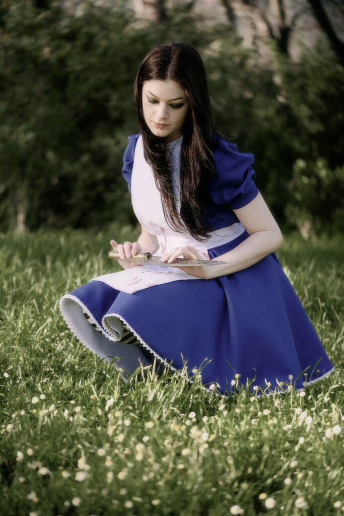 Alice cosplayer from Alice madness returns crouched in a field of flowers