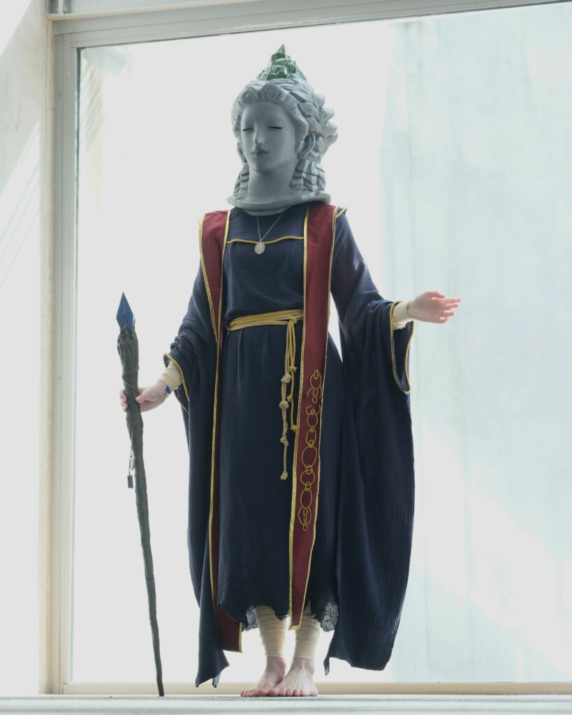 Sellen cosplayer standing by a window hold a staff