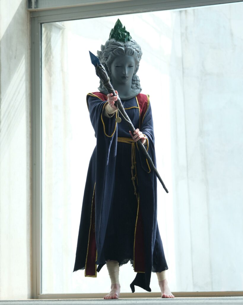 Sellen cosplayer standing by a window hold a staff at camera