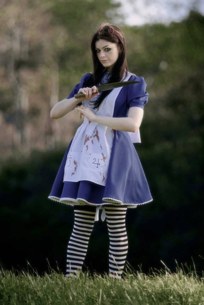 Alice cosplayer from Alice madness standing in field with a knife